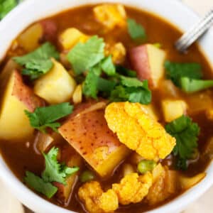 Curried cauliflower potato soup with cilantro in white bowl.