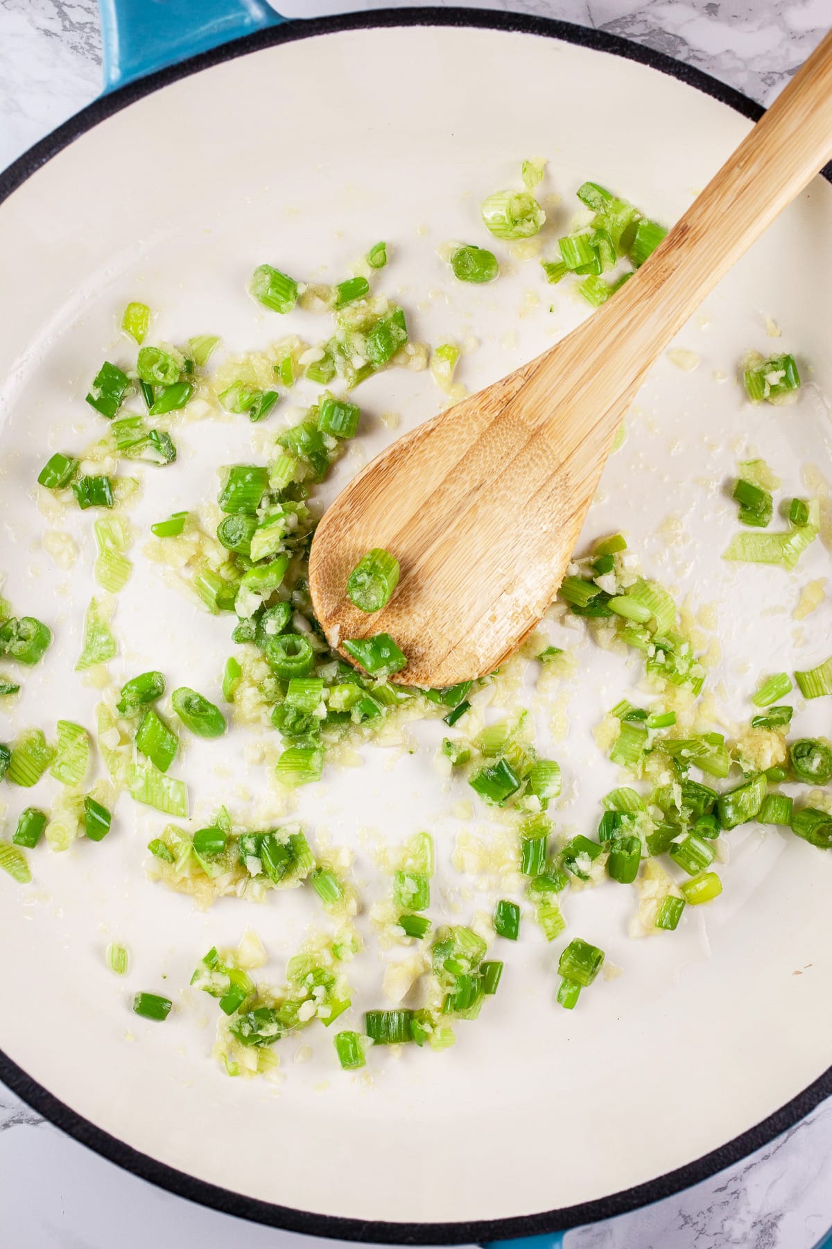 Garlic, scallions, and ginger sautéed in skillet with wooden spoon.