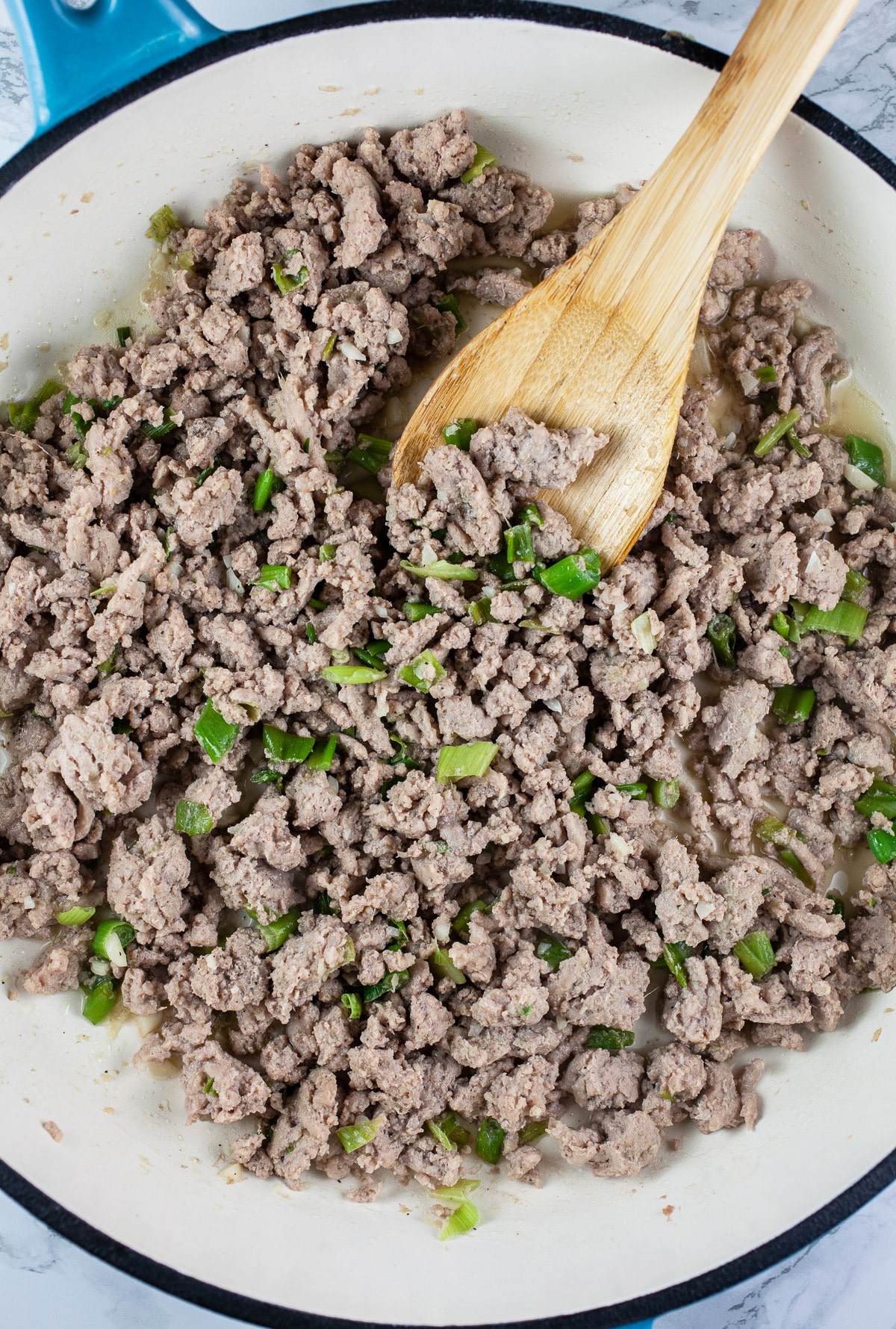 Garlic, scallions, ginger, and ground turkey sautéed in skillet with wooden spoon.