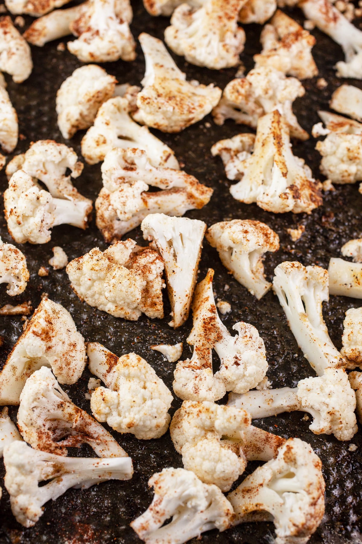 Cauliflower florets tossed in olive oil and spices on sheet pan.