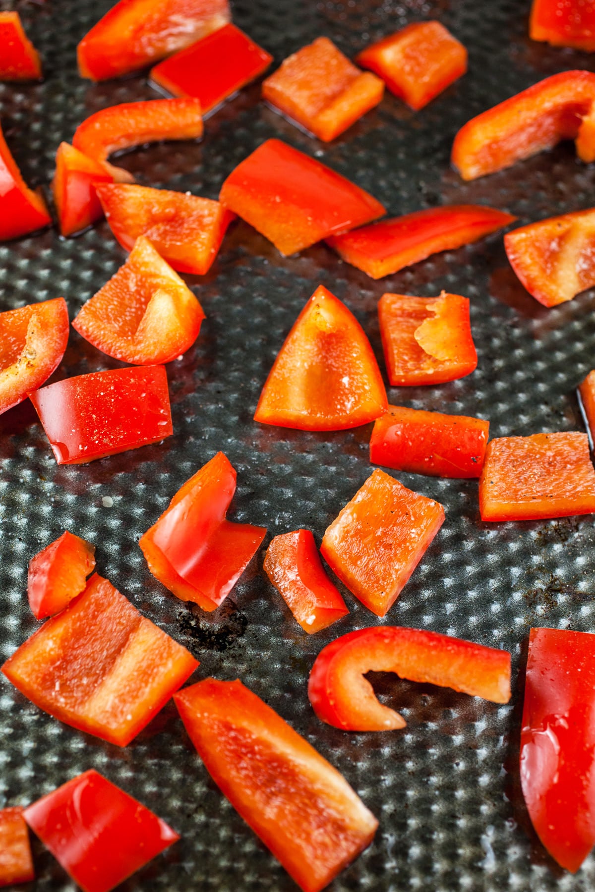 Bell pepper chunks tossed in olive oil on baking sheet.