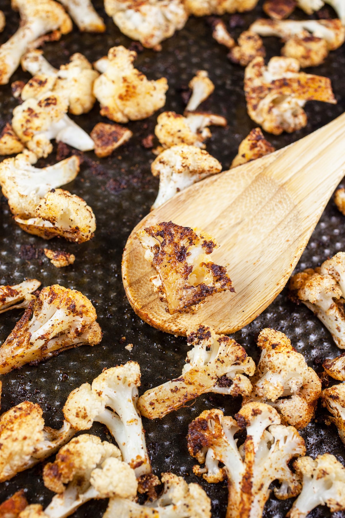 Roasted cauliflower with wooden spoon on baking sheet.