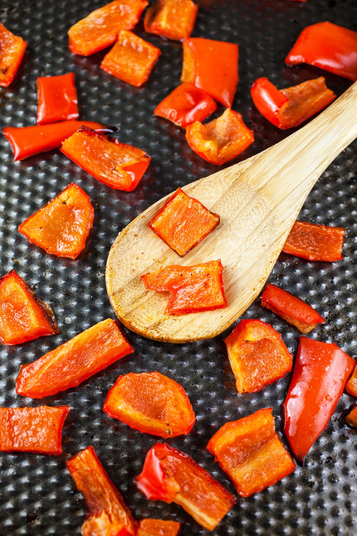Roasted red bell peppers with wooden spoon on baking sheet.