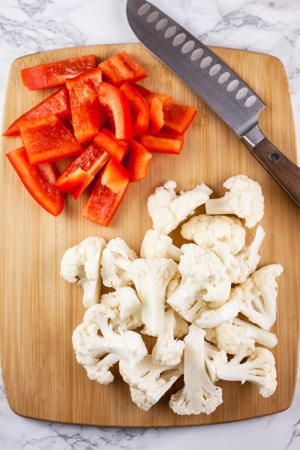 Cauliflower florets and red bell pepper slices on wooden cutting board.