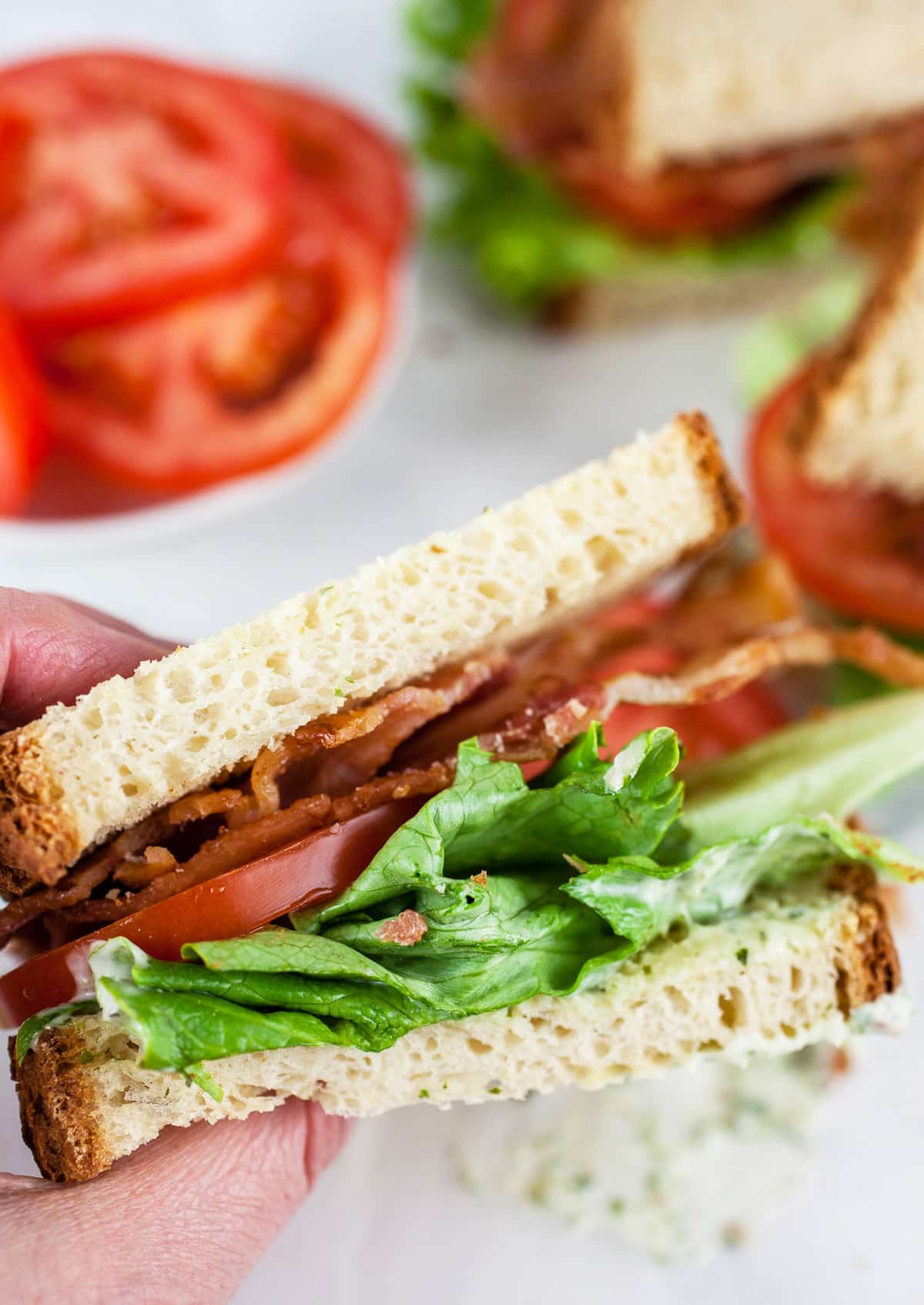 Hand holding half a BLT sandwich.