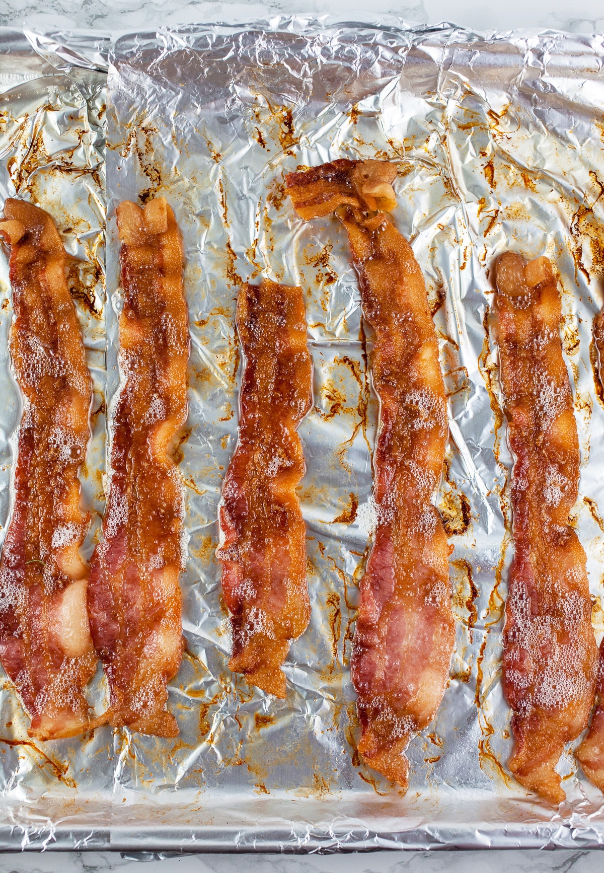 Cooked bacon on aluminum foil lined baking sheet.