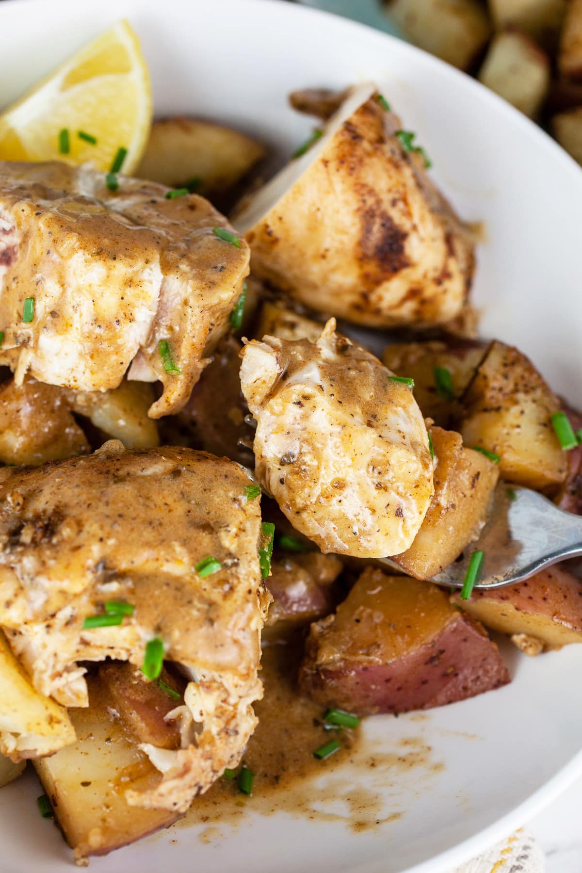 Chicken breasts, red potatoes, and pan sauce in white bowl with fork.