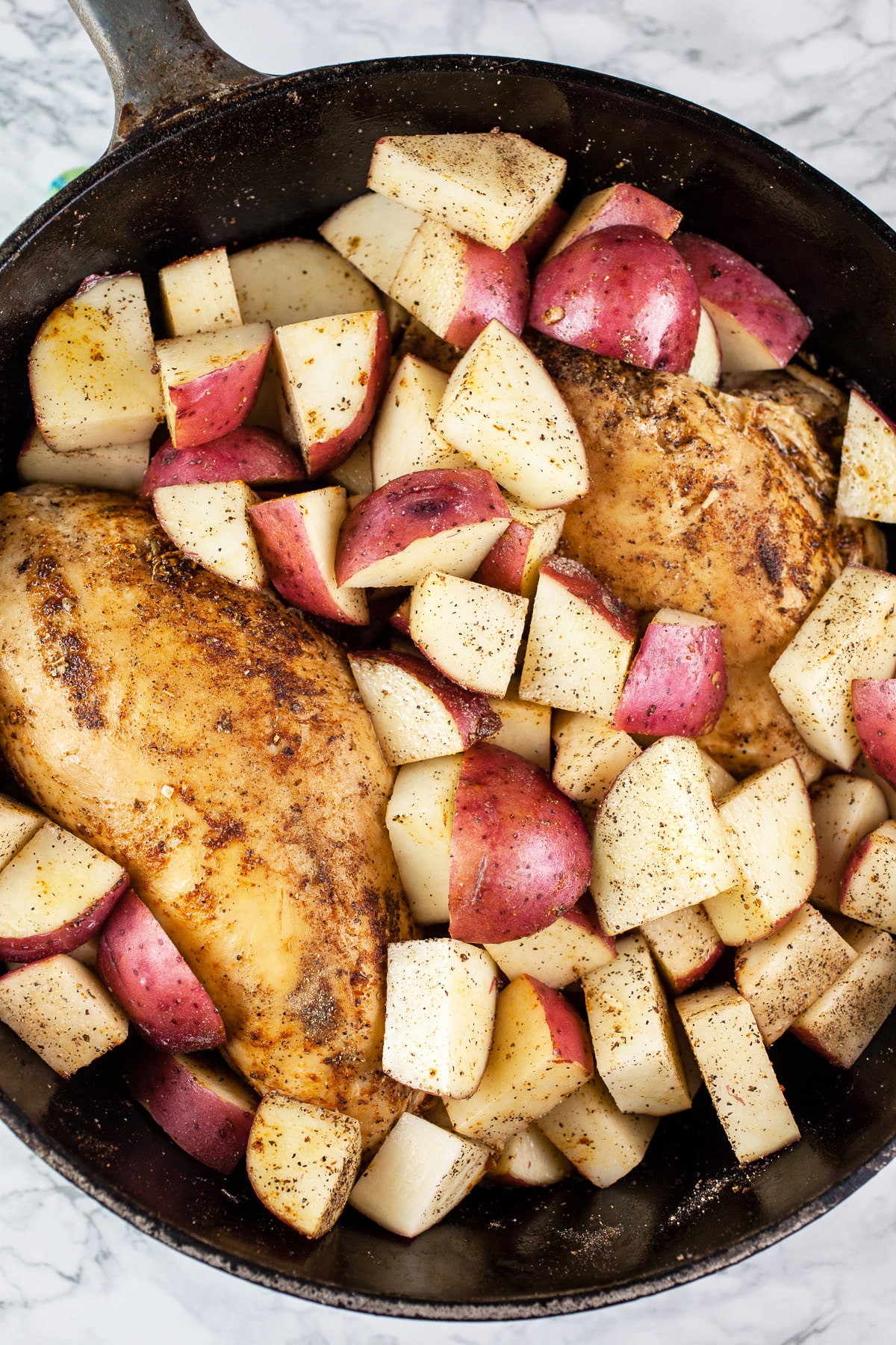 Uncooked chicken breasts and red potatoes in Dutch oven.