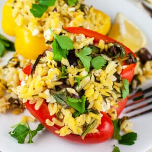 Vegetarian Greek stuffed peppers with orzo, Kalamata olives, and parsley on white plate.