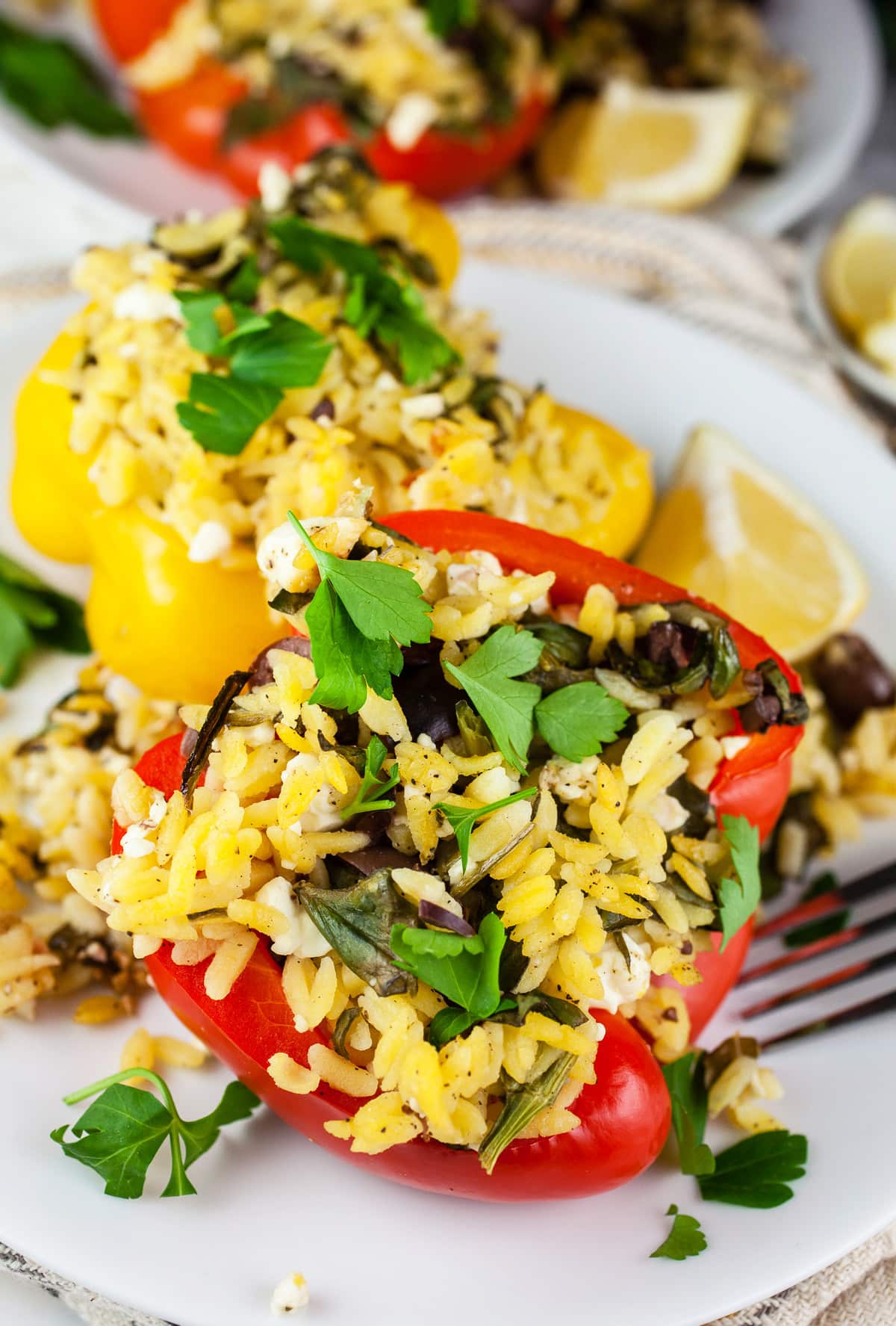 Greek stuffed peppers with parsley and lemon wedges on white plates.