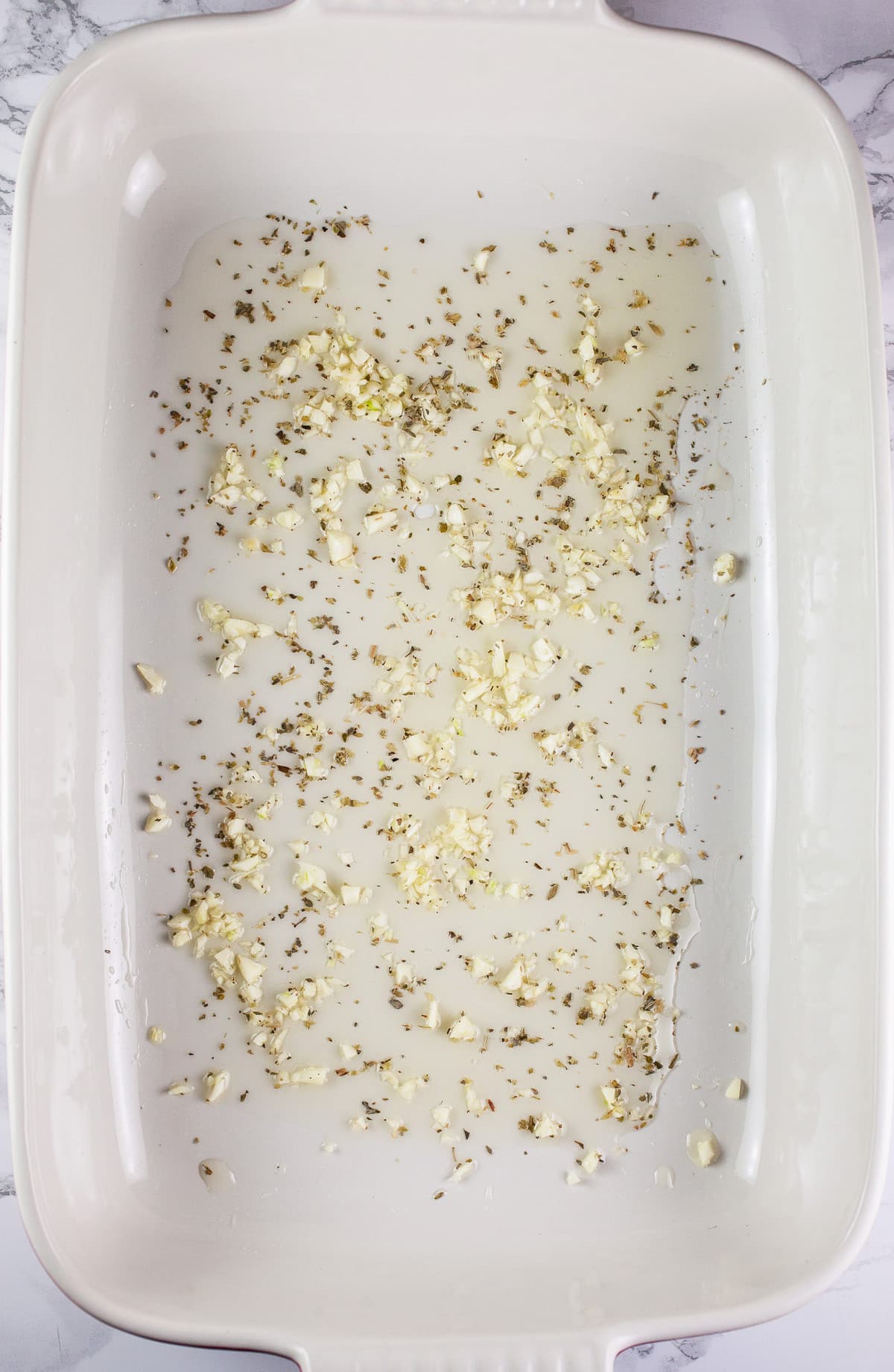 Minced garlic, olive oil, and dried oregano in ceramic baking dish.