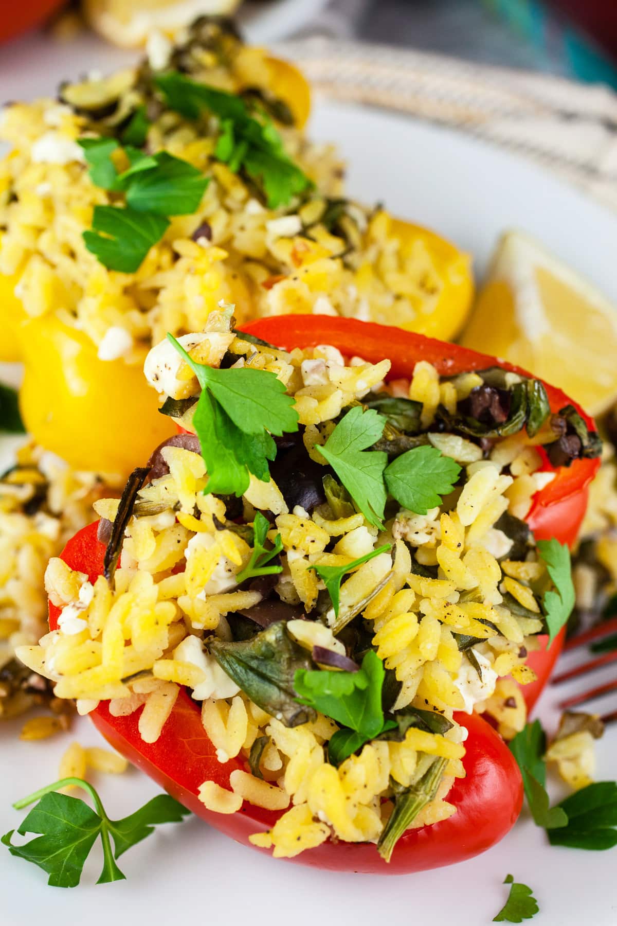 Vegetarian Greek stuffed peppers with orzo, feta cheese, Kalamata olives, and parsley on white plate.