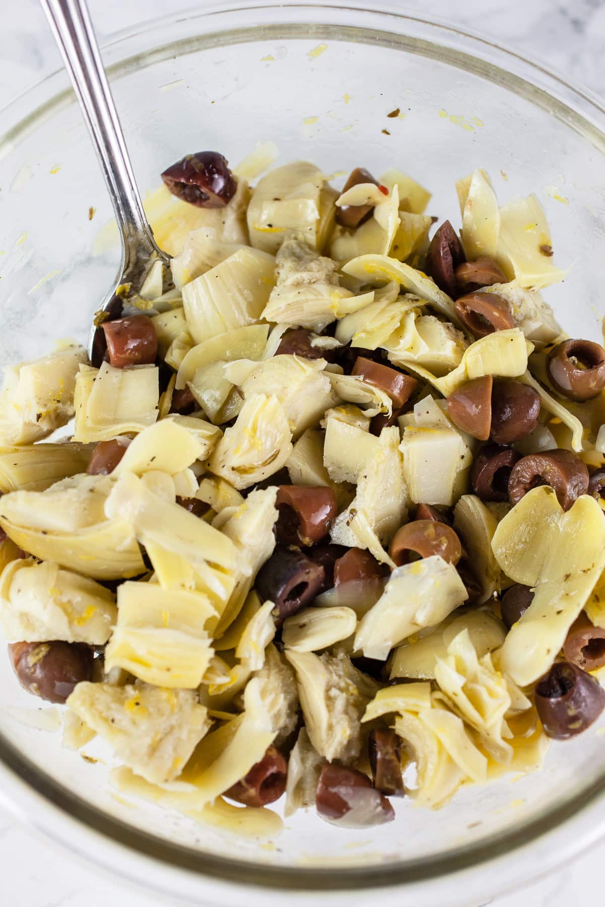 Marinated artichoke hearts and chopped Kalamata olives mixed together in glass bowl.