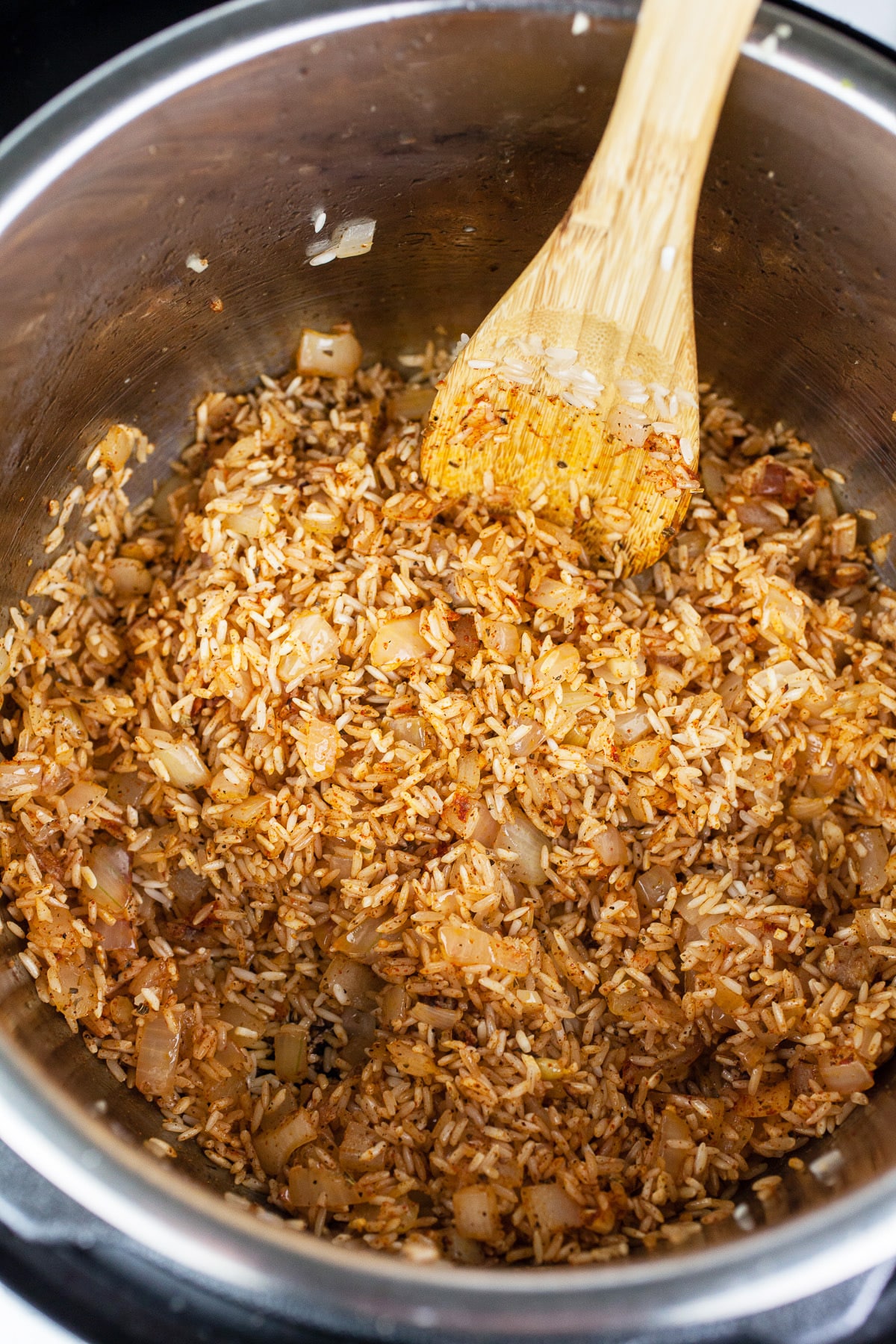 Rice and spices sautéed in Instant Pot with wooden spoon.