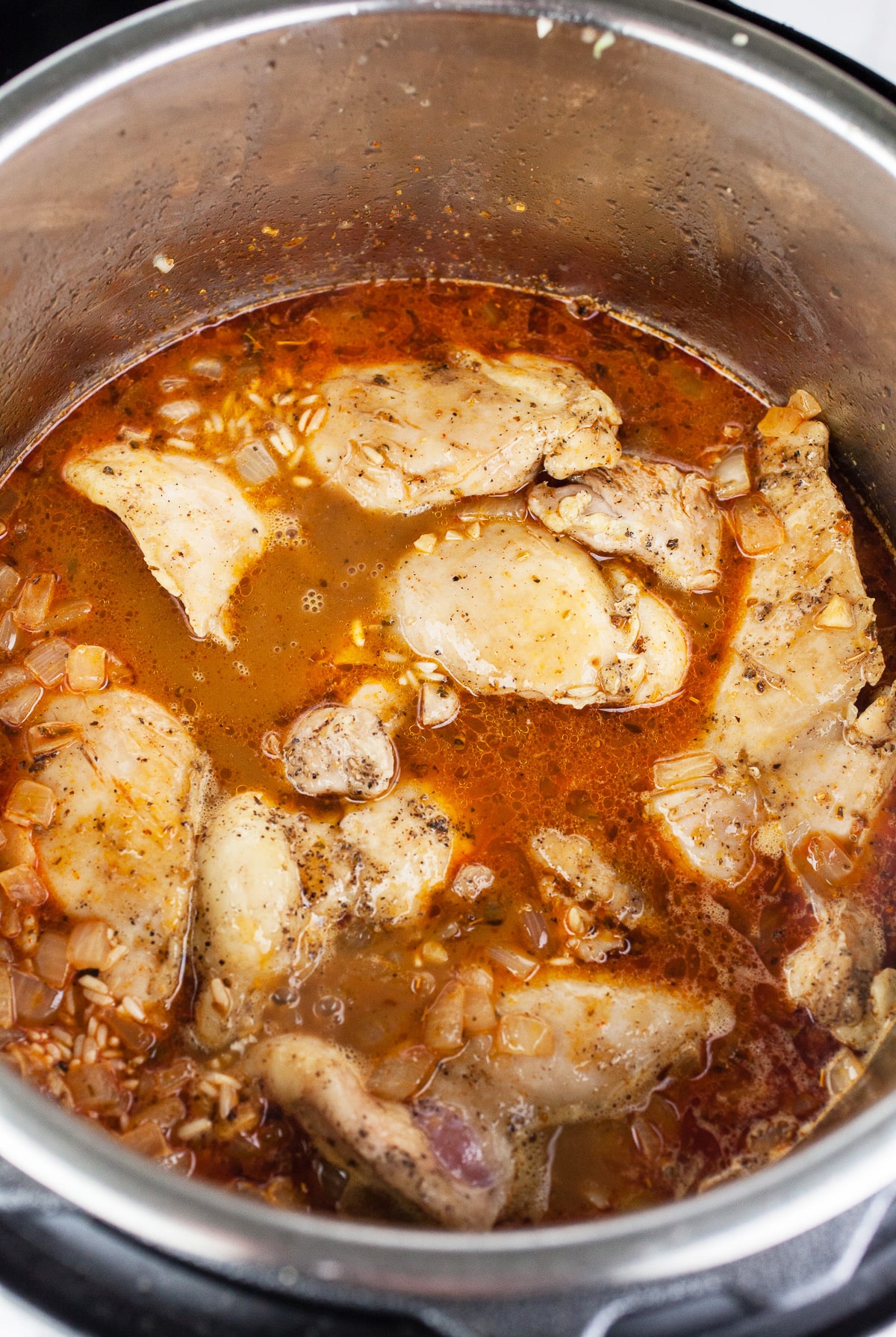 Uncooked chicken thighs and broth in Instant Pot.