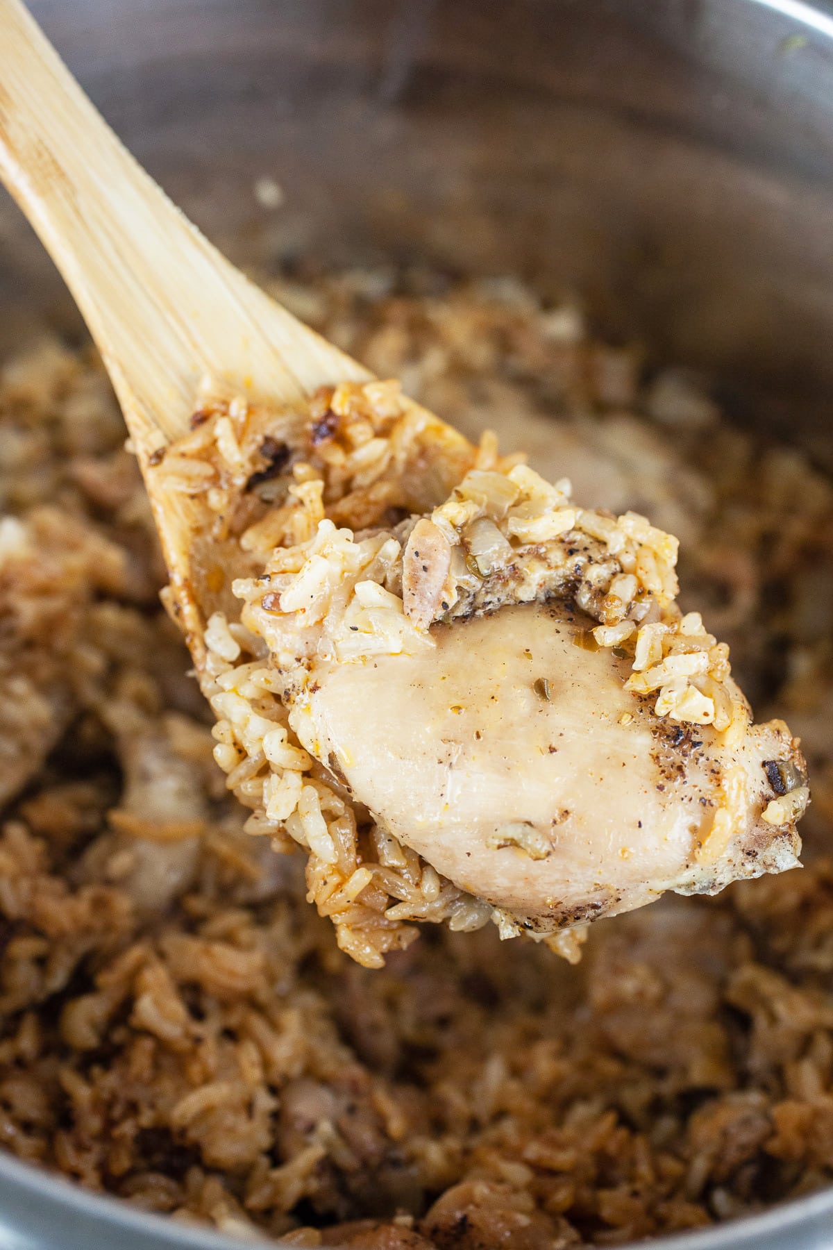 Cooked chicken thigh lifted from Instant Pot on wooden spoon.