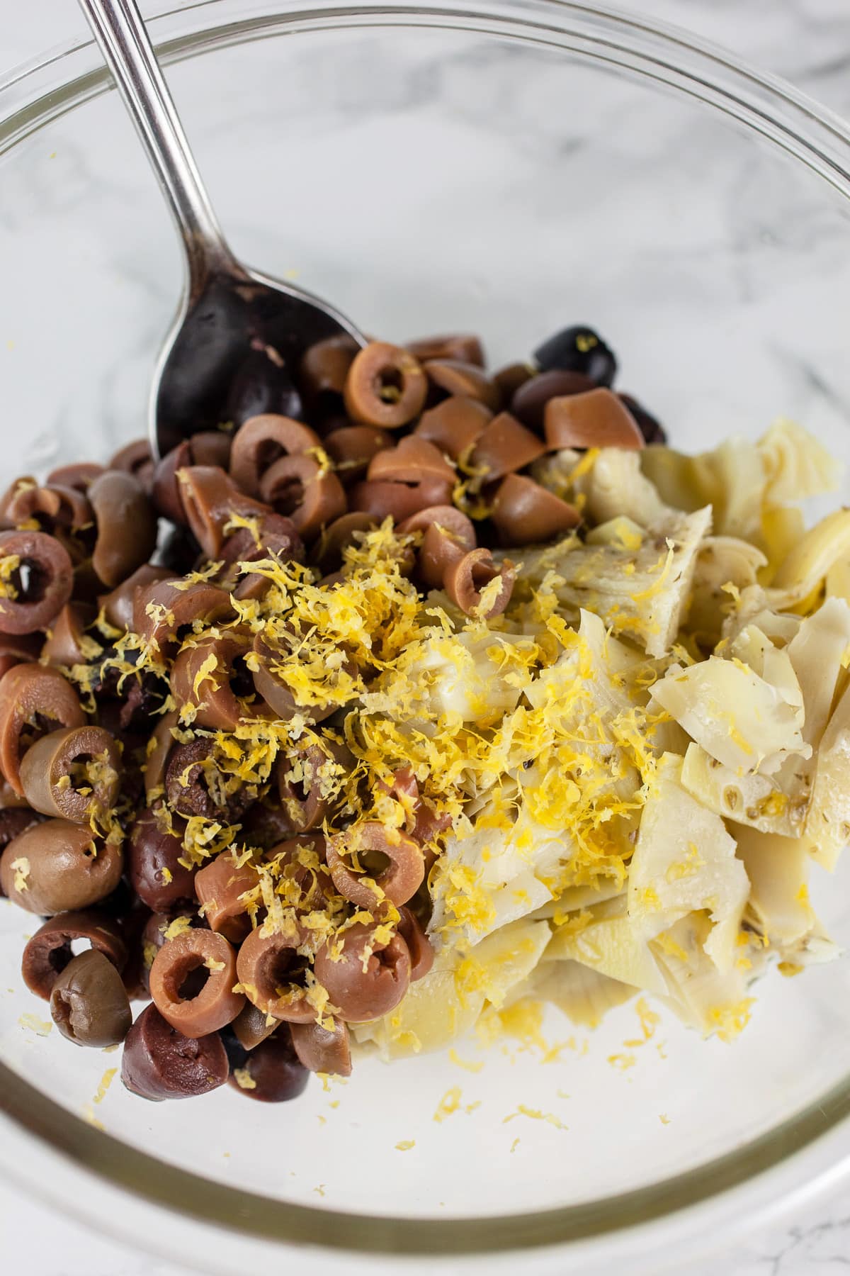 Marinated artichoke hearts, Kalamata olives, and lemon zest in glass bowl.