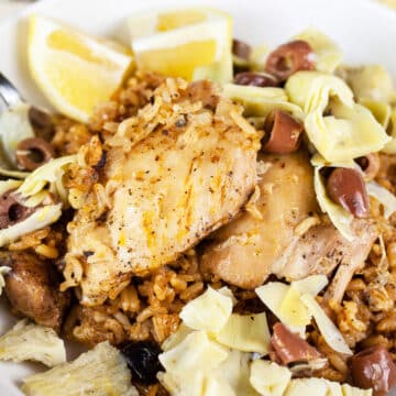 Mediterranean chicken thighs and rice with artichokes, Kalamata olives, and lemon wedges.