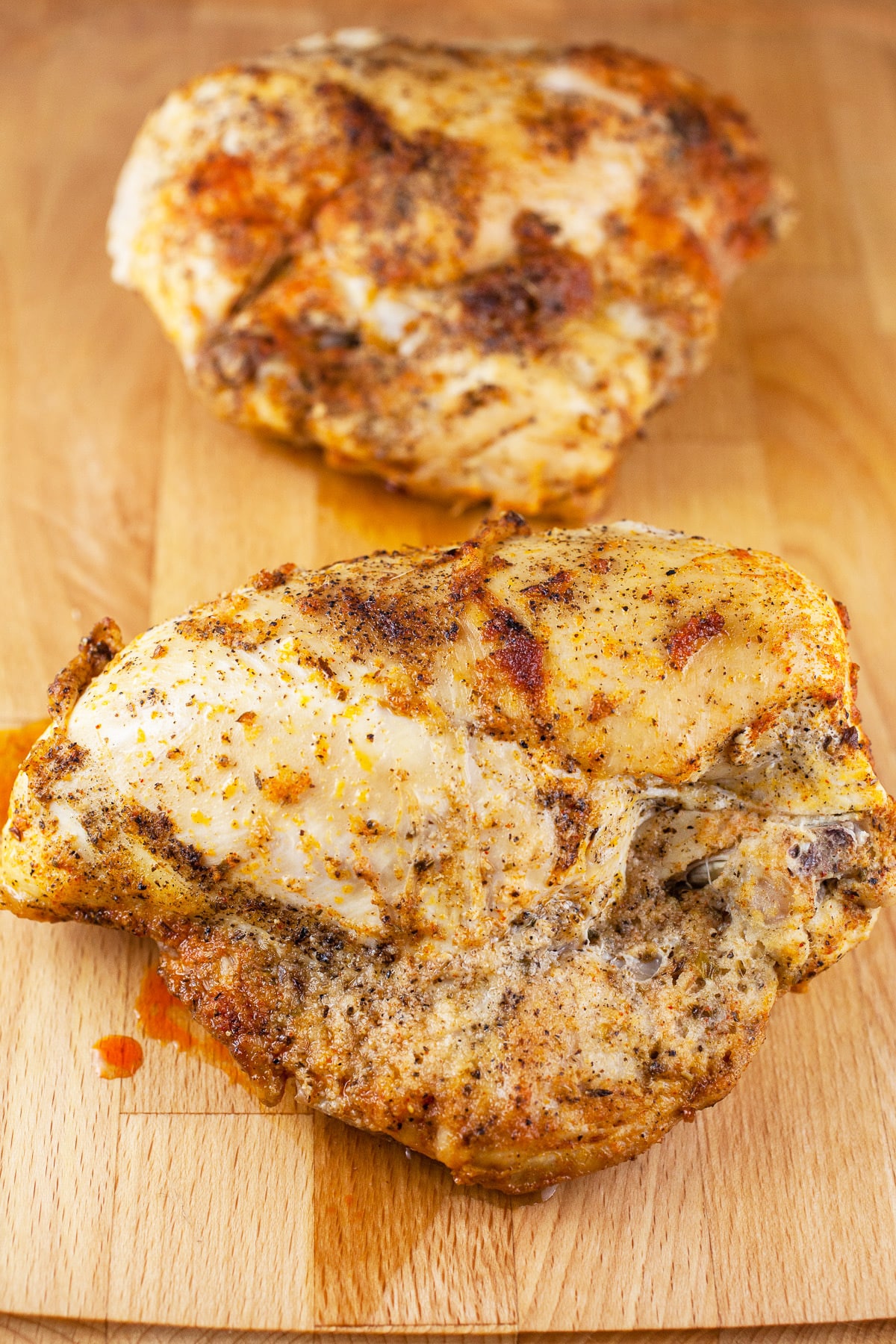 Cooked split chicken breasts on wooden cutting board.