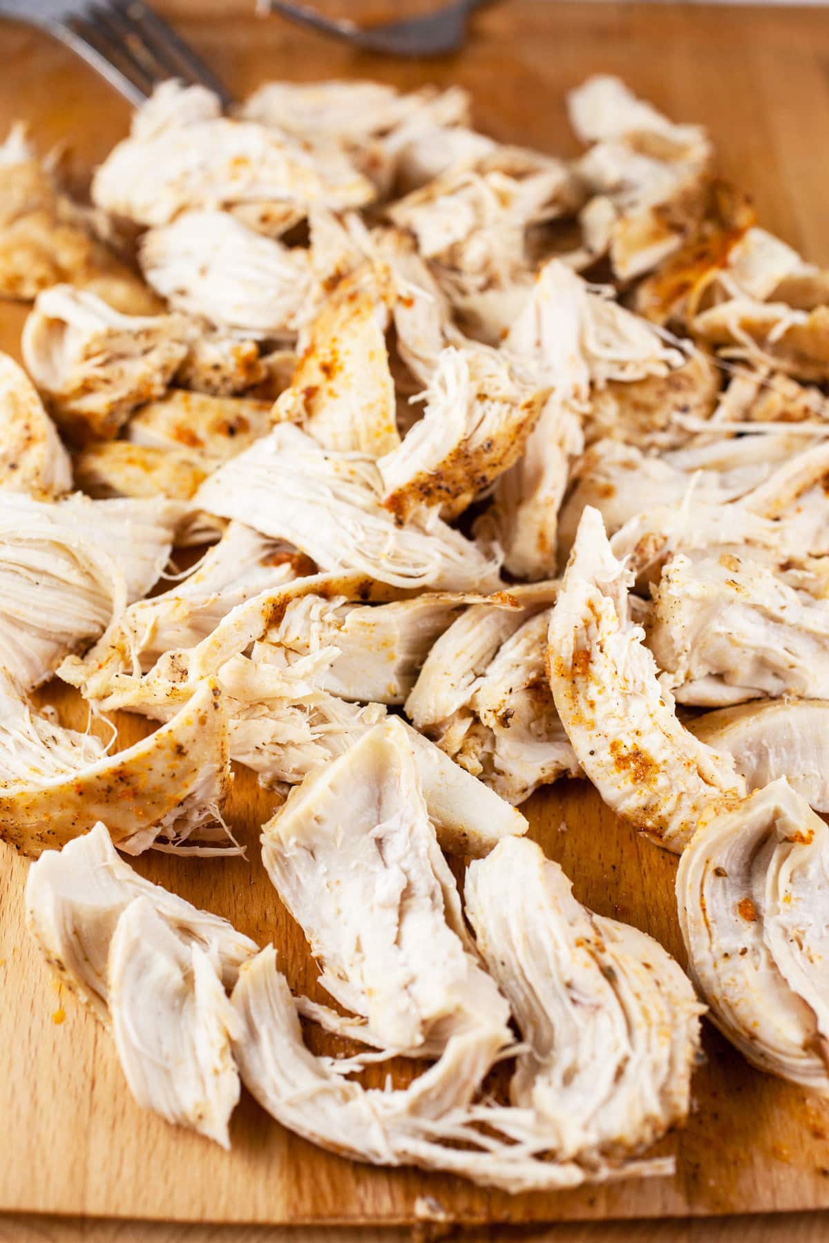 Shredded cooked chicken breasts on wooden cutting board.