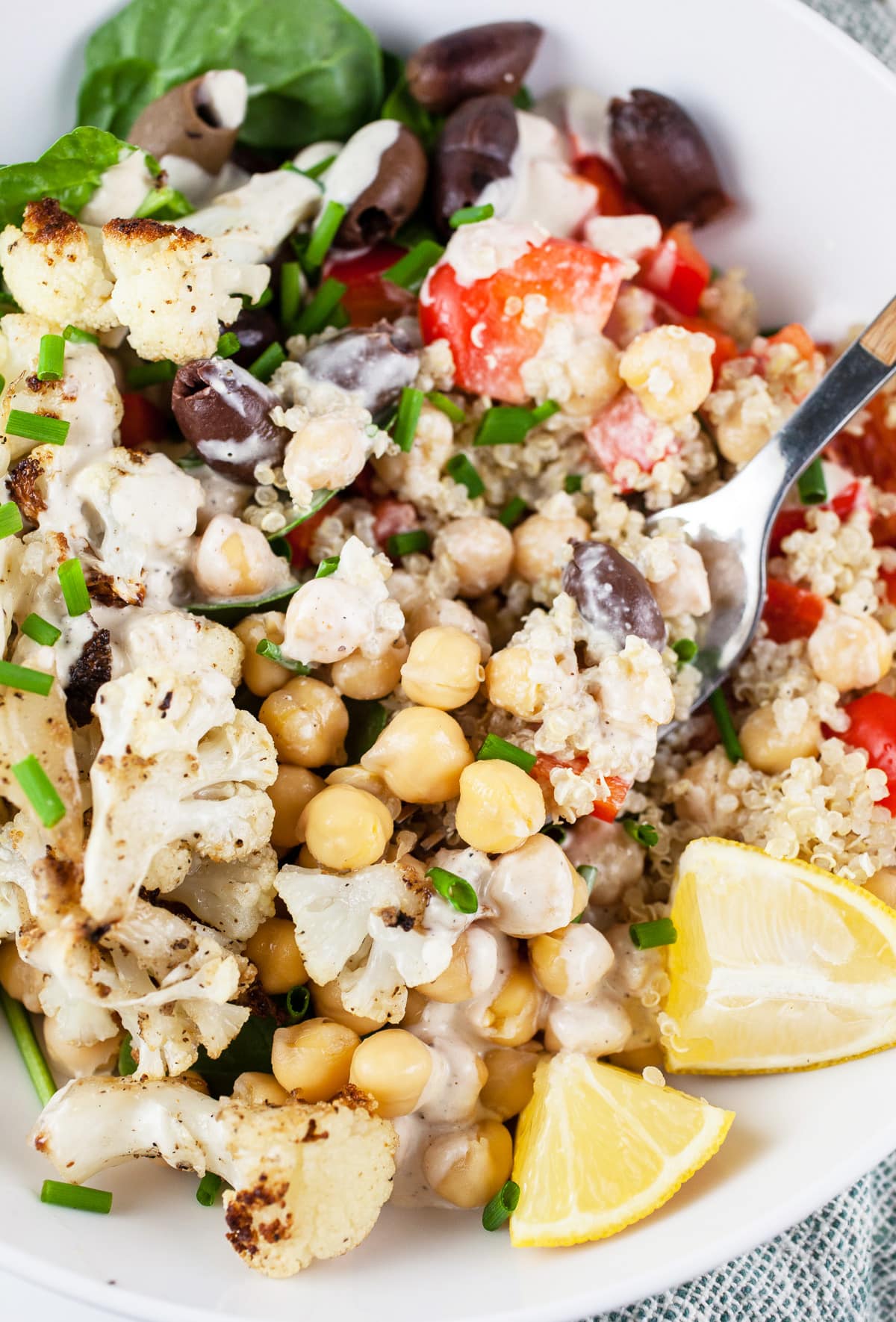Mediterranean chickpea quinoa bowl with Kalamata olives, red bell peppers, tahini dressing, and lemon wedges.