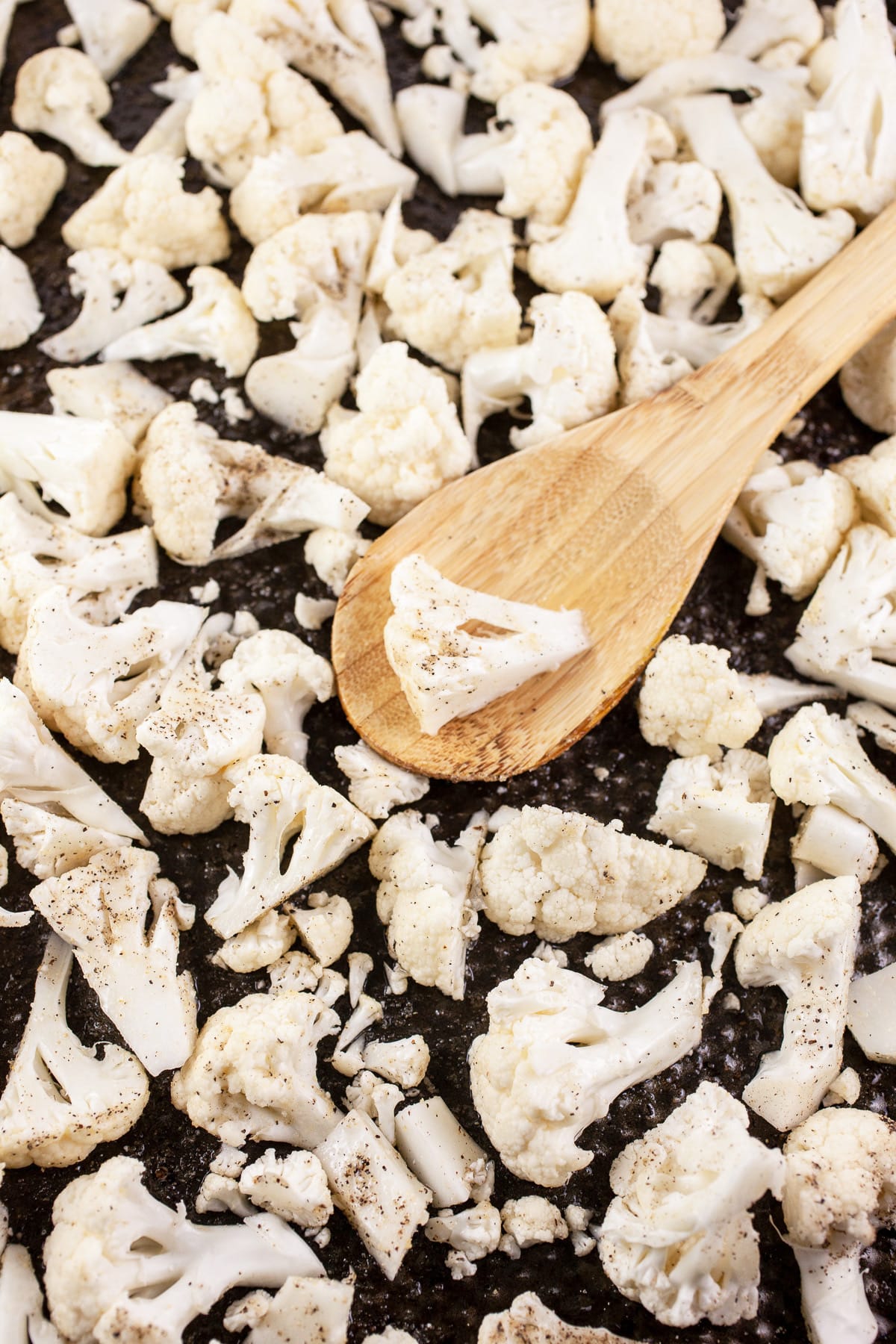 Uncooked cauliflower florets on baking sheet with wooden spoon.