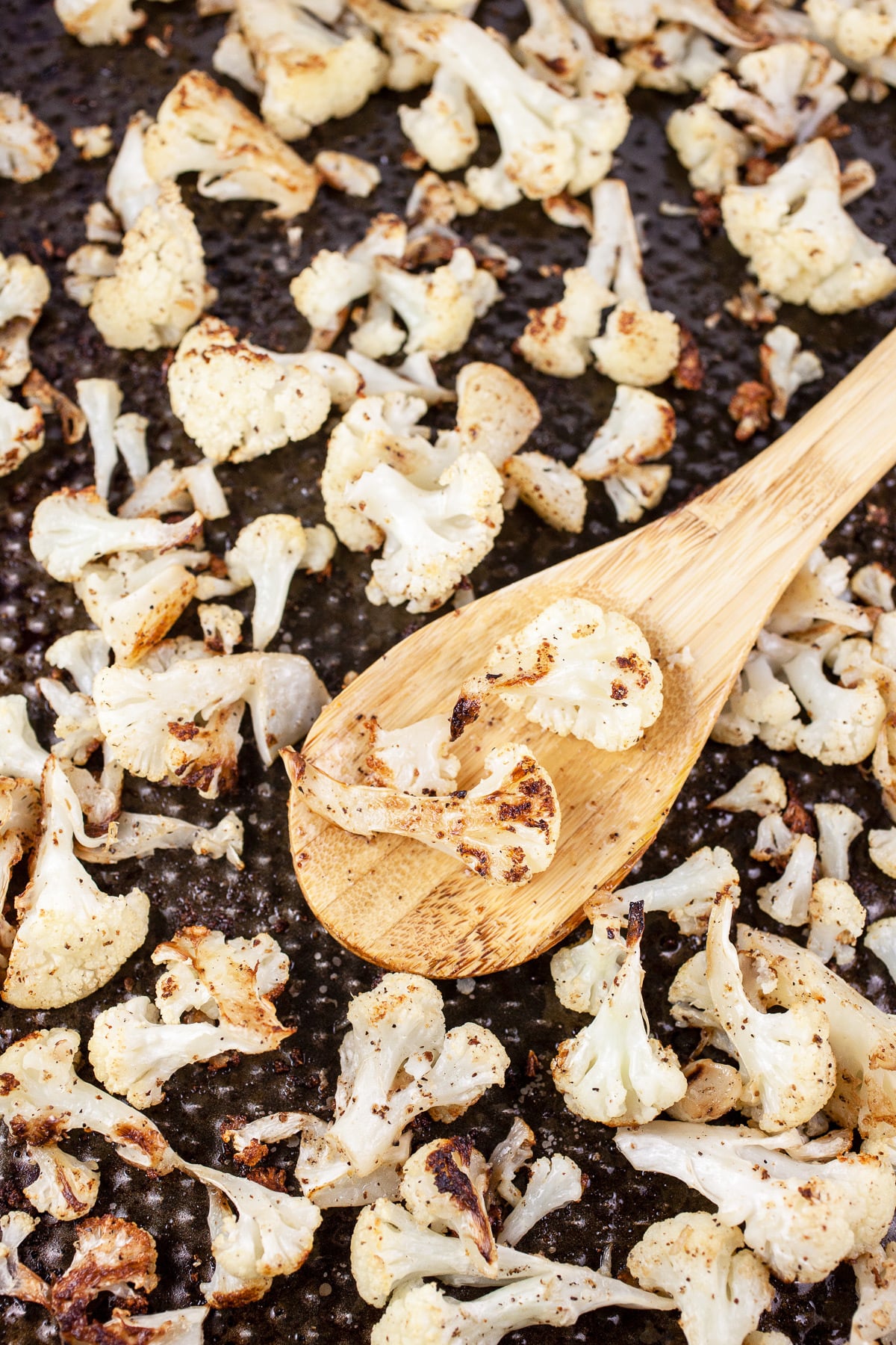 Roasted cauliflower florets on baking sheet with wooden spoon.
