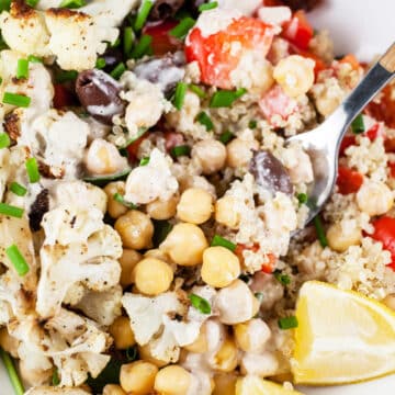 Mediterranean chickpea quinoa bowl with cauliflower, Kalamata olives, peppers, and lemon wedge.