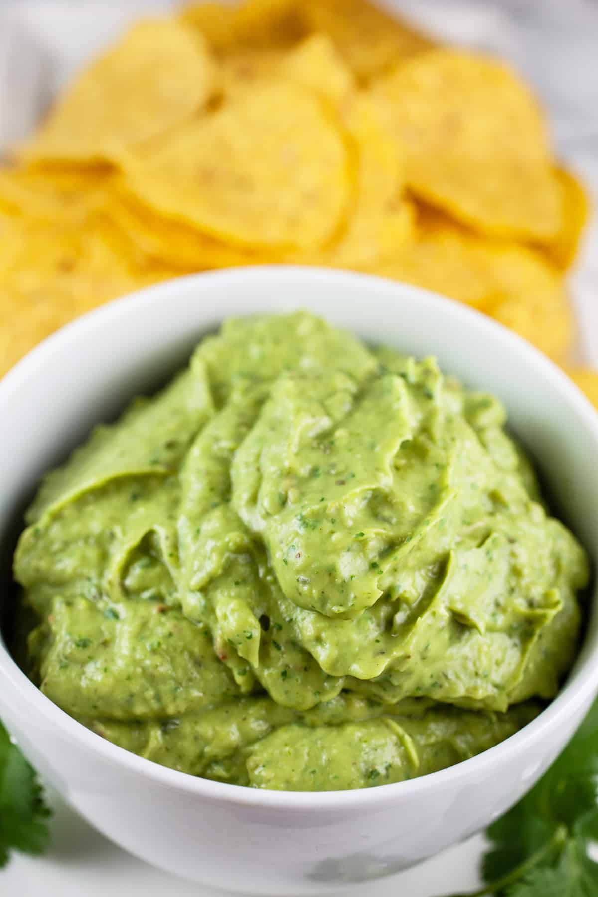 Poblano avocado sauce in white bowl with round tortilla chips.