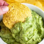 Tortilla chip dipped into white bowl of poblano avocado sauce.