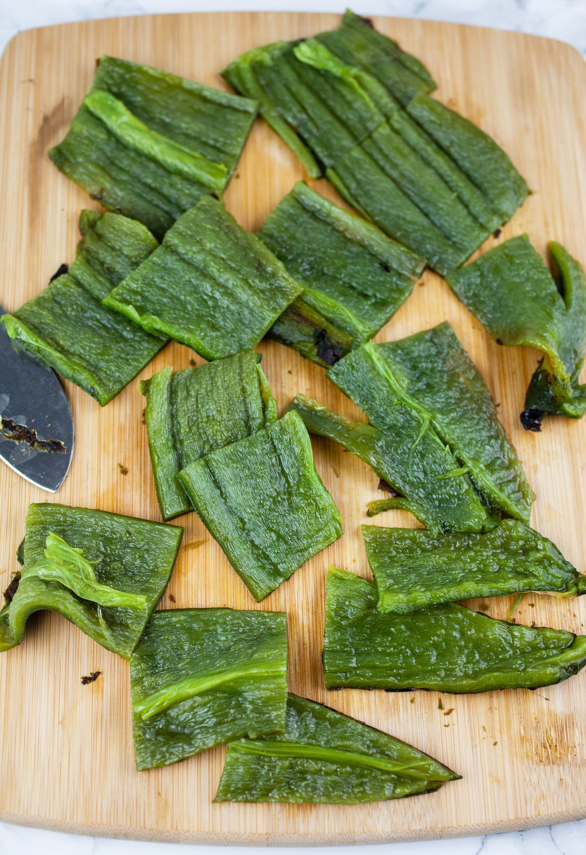 Roasted poblano peppers cut into chunks on wooden cutting board.