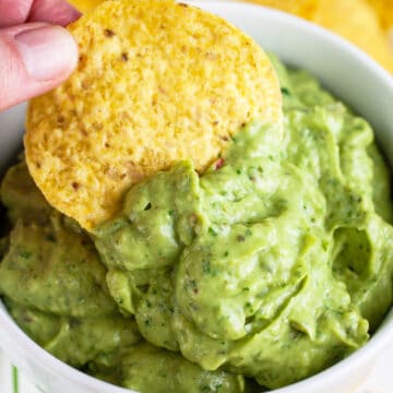 Tortilla chip dipped into white bowl of poblano avocado sauce.