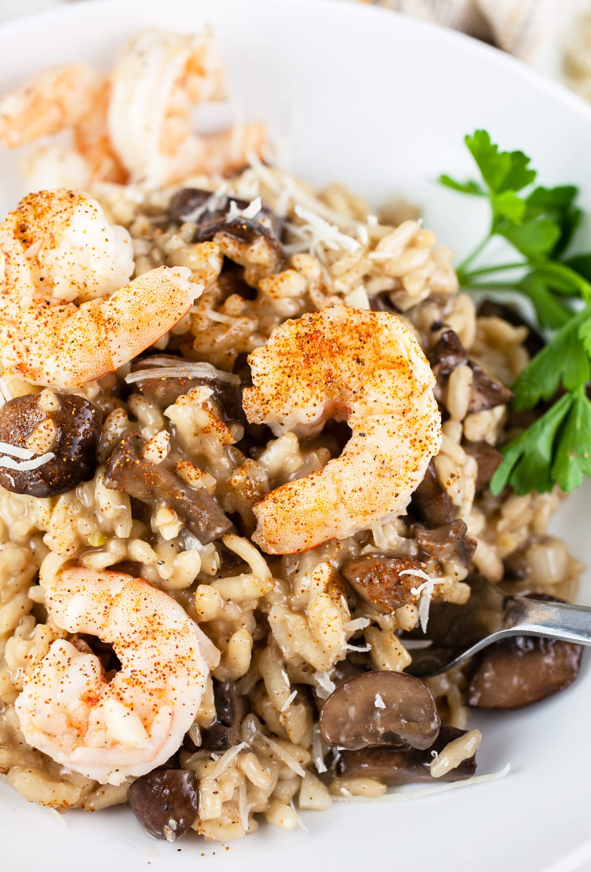 This Garlicky Mushroom and Shrimp Risotto makes the perfect simple and elegant dinner for two! Creamy risotto is tossed with mushrooms that have cooked in garlic and onions. The dish is topped with succulent shrimp and Parmesan cheese. This is one of my favorite easy seafood recipes. Risotto is a dish that's easy to prepare but seems fancy. Impress your guests with this dinner! #risotto #mushroom #shrimp #garlic #recipes #Italian Mushroom shrimp risotto with parsley in white bowl.