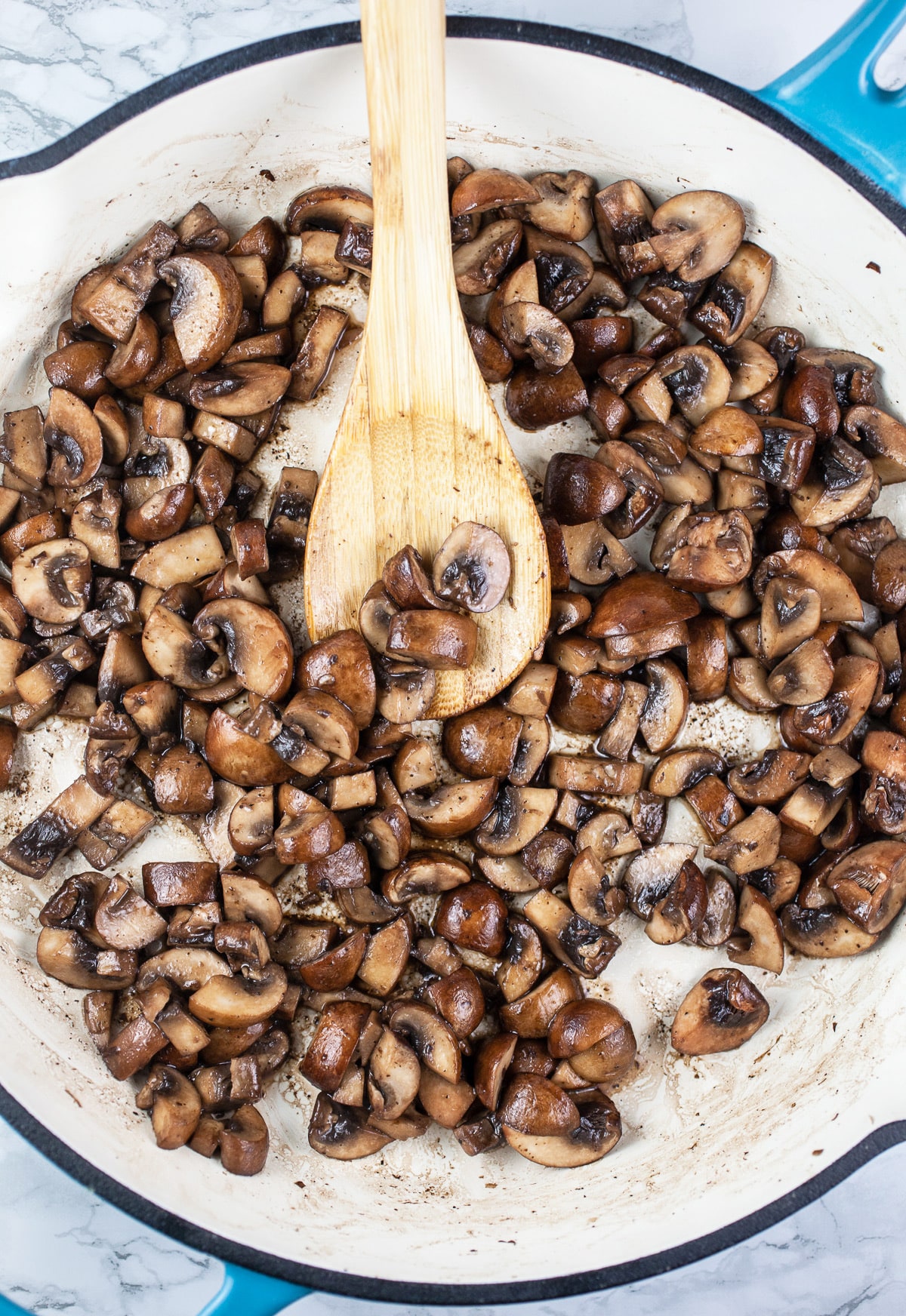 Sautéed mushrooms in skillet with wooden spoon.