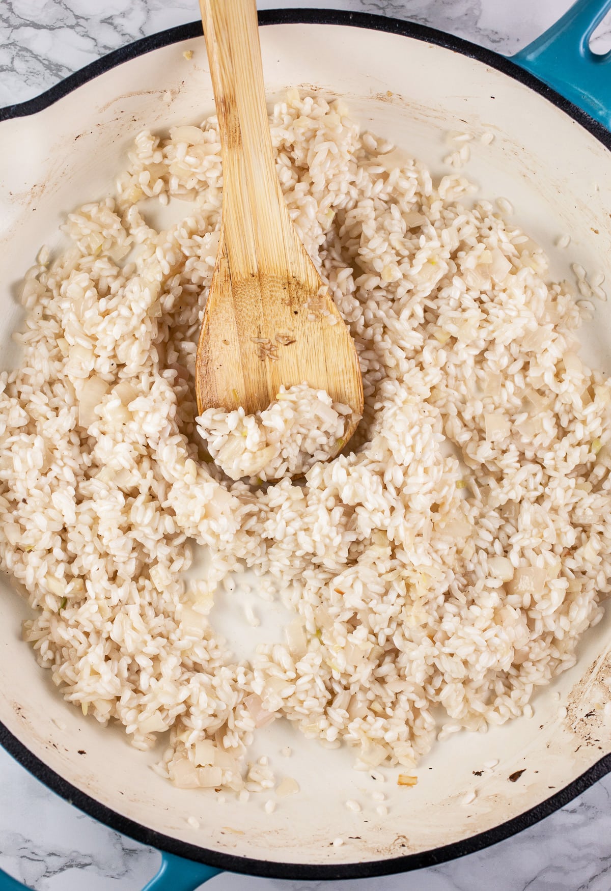 Garlic, shallots, Arborio rice, and white wine sautéed in skillet with wooden spoon.