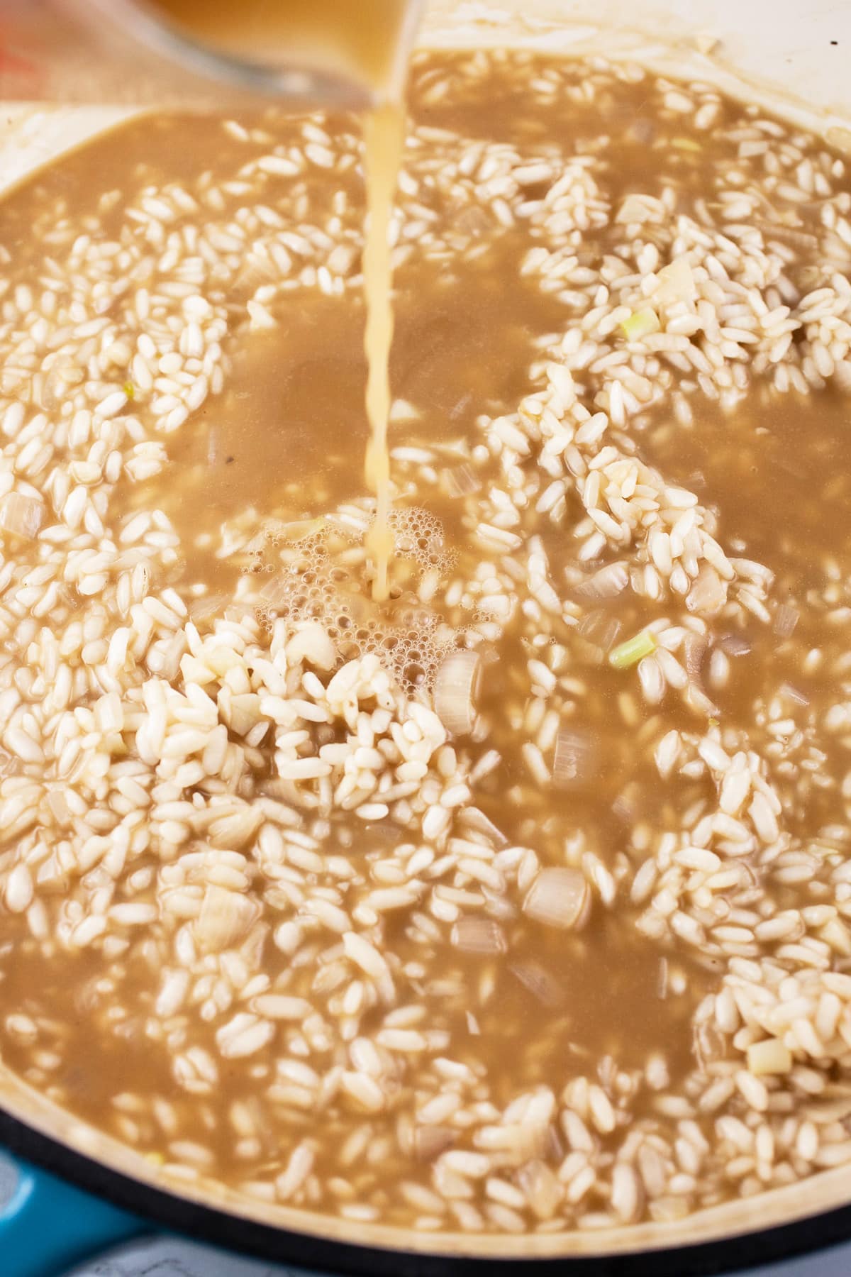 Chicken broth poured into skillet of Arborio rice being cooked.