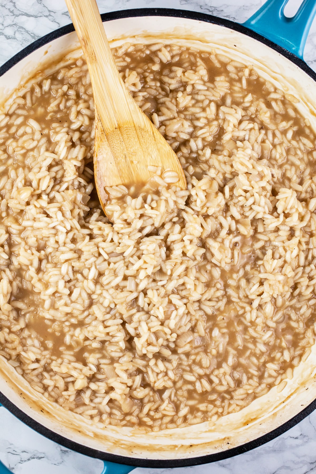 Arborio rice cooked in skillet with wooden spoon.