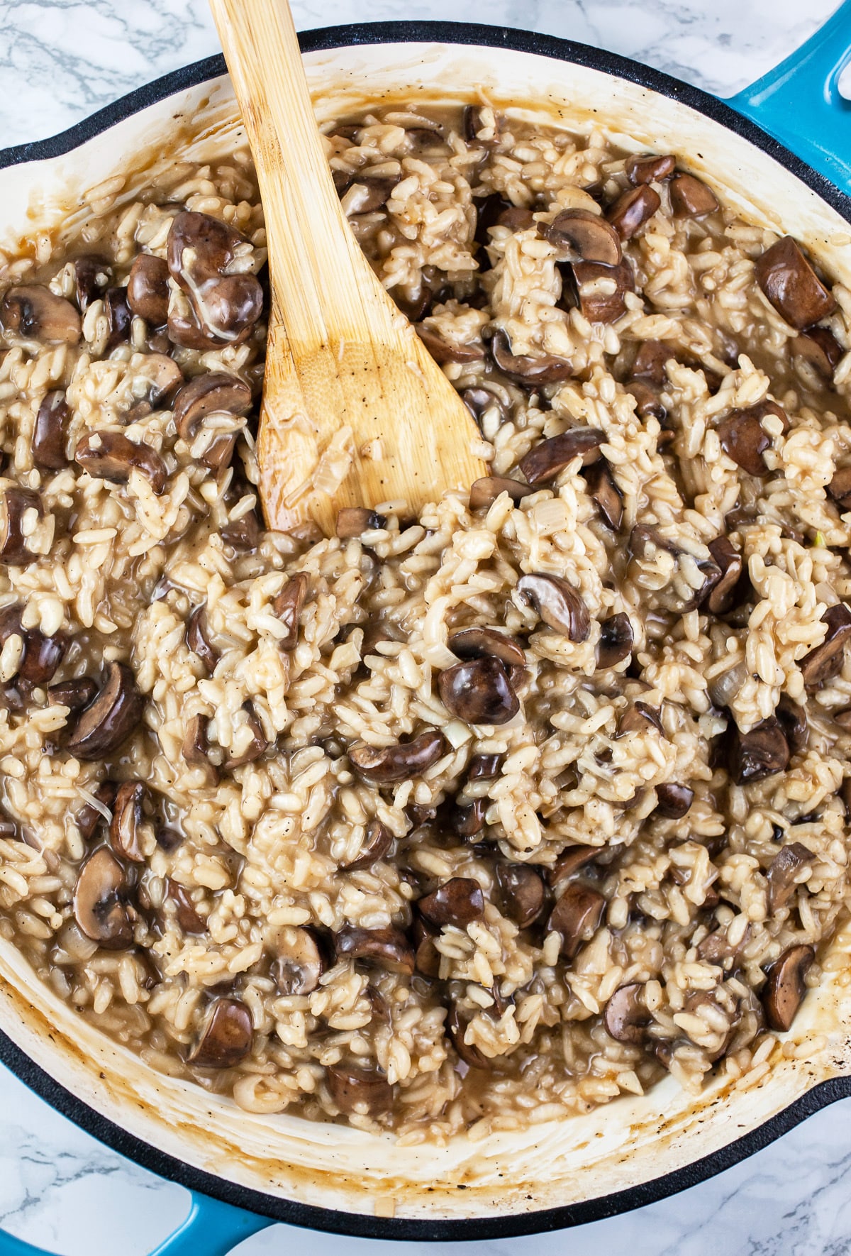 Mushroom risotto in skillet with wooden spoon.