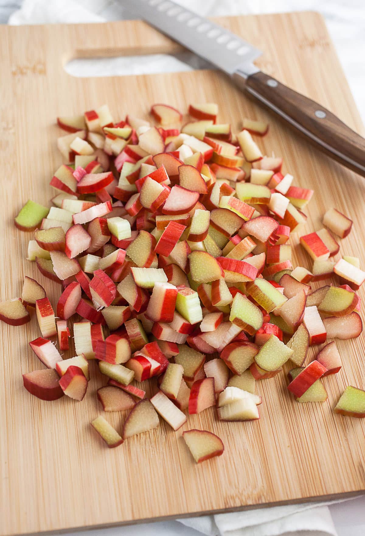 Chopped rhubarb on wooden cutting board with knife.