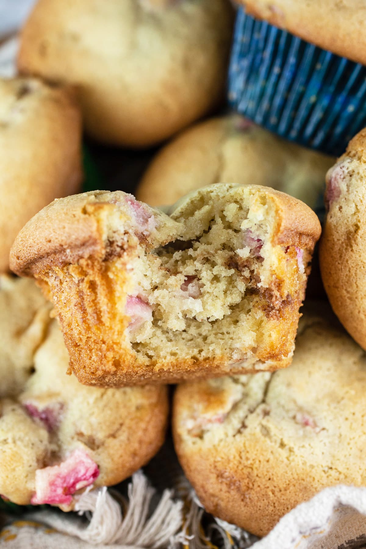 Bite taken from rhubarb muffin sitting in a bowl of muffins.