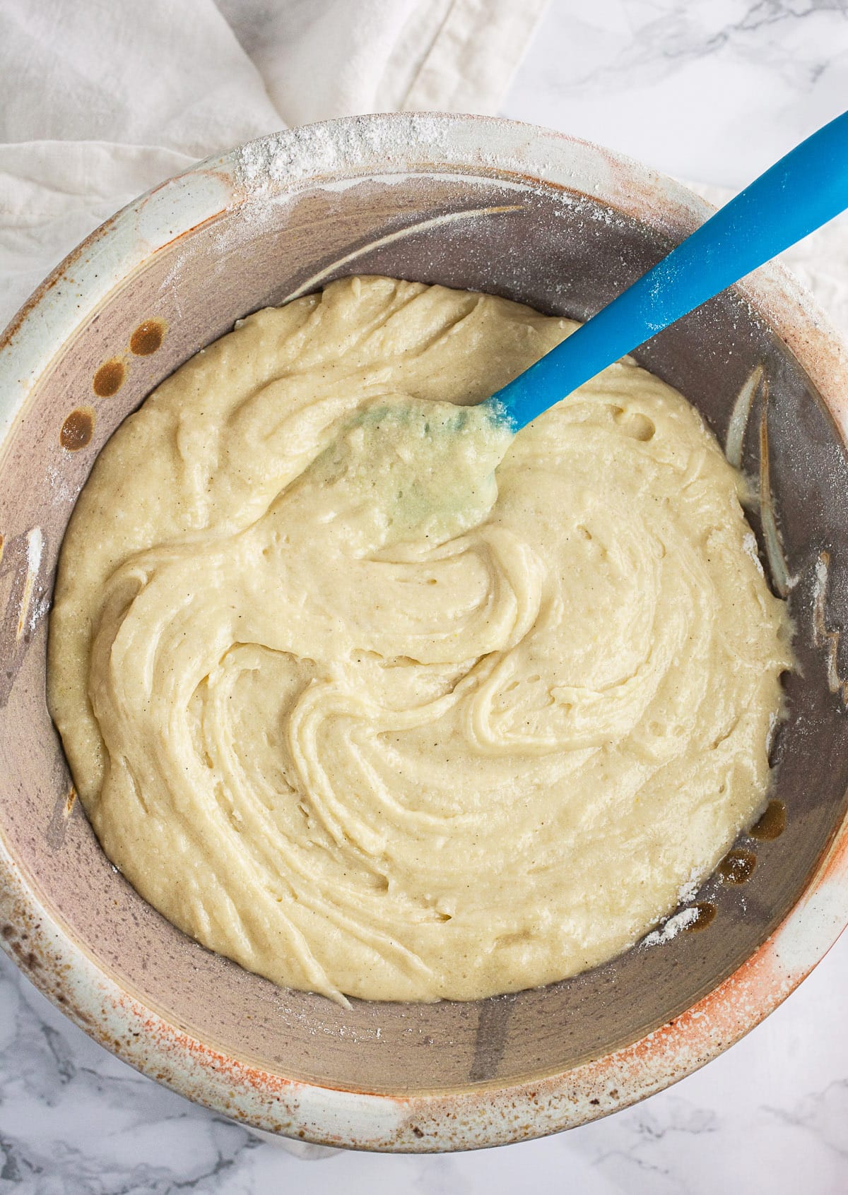 Muffin batter in ceramic bowl with blue spatula.