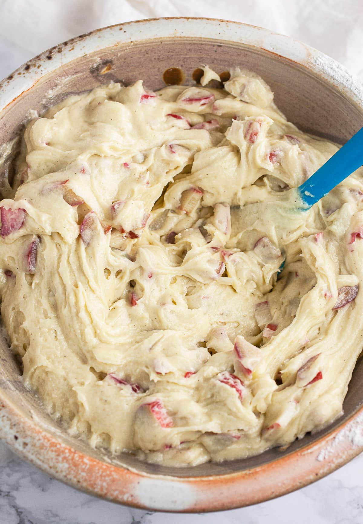 Rhubarb muffin batter in ceramic bowl with blue spatula.