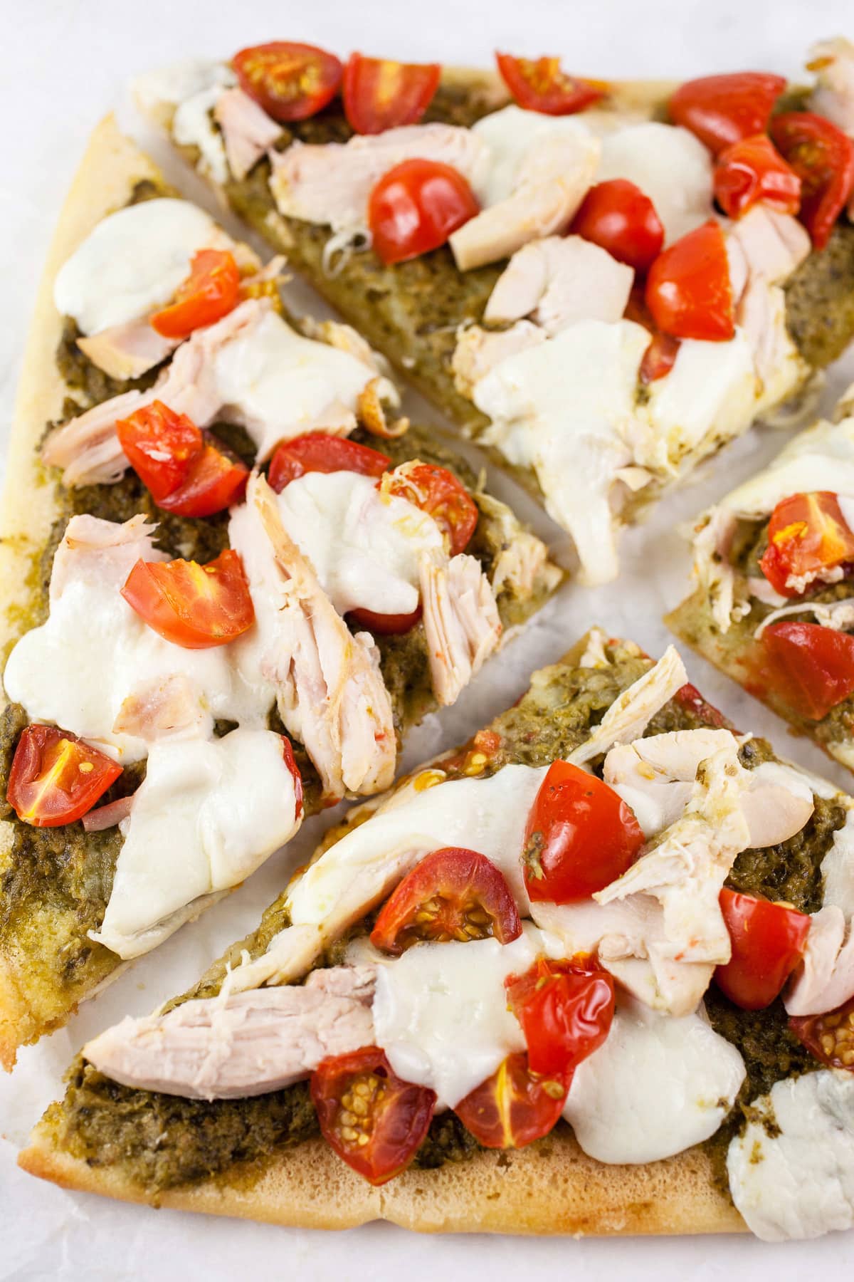 Cooked chicken pesto flatbread cut into slices on white surface.