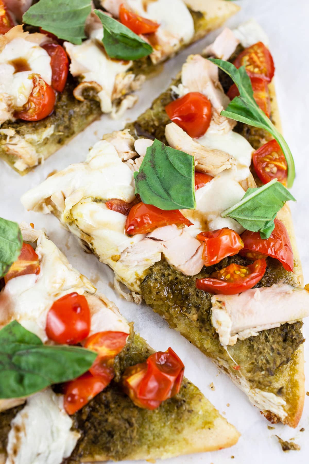 Pesto chicken flatbread with fresh basil cut into slices.