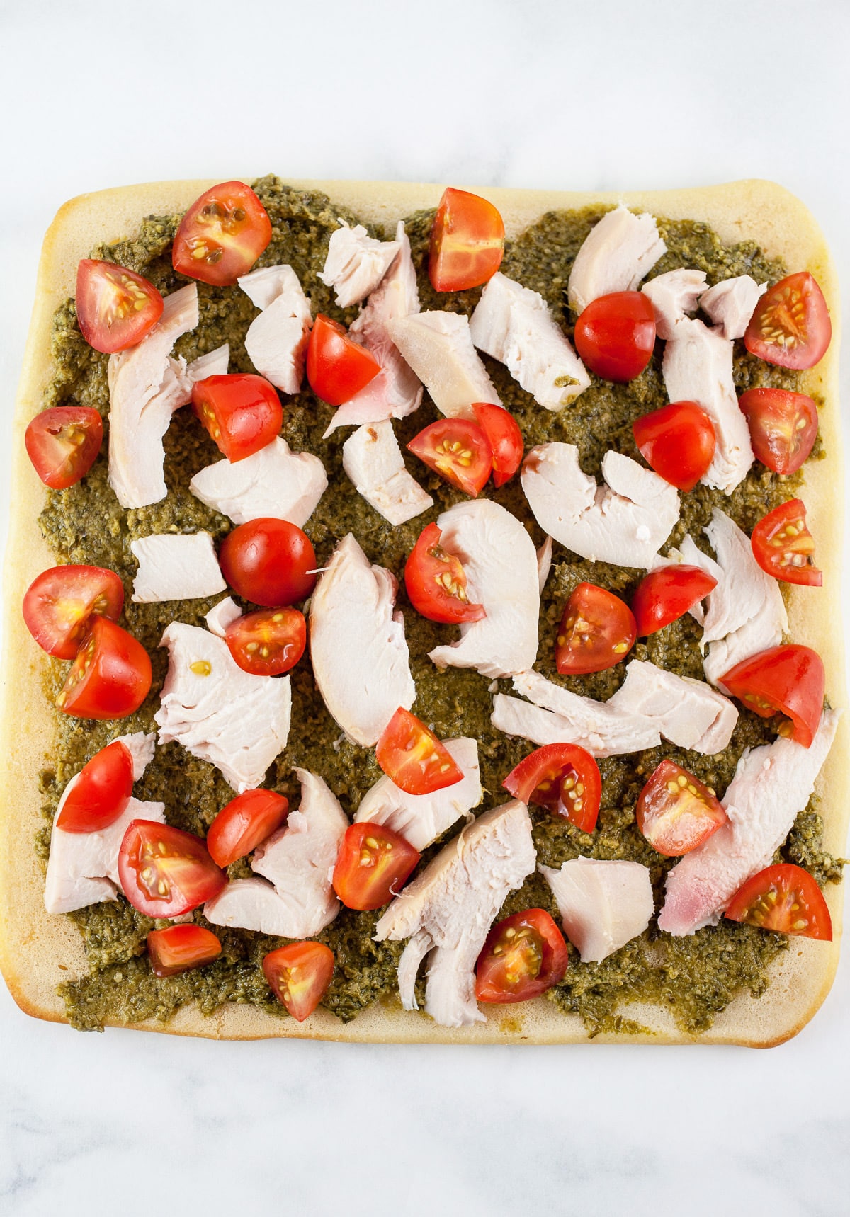 Basil pesto, shredded chicken, and diced cherry tomatoes on flatbread.