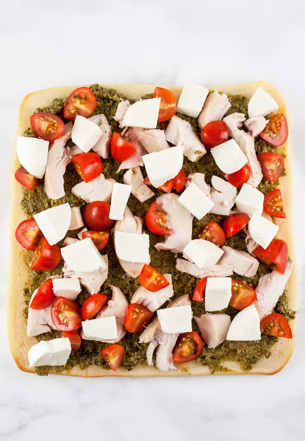 Basil pesto, shredded chicken, diced cherry tomatoes, and fresh mozzarella on flatbread.