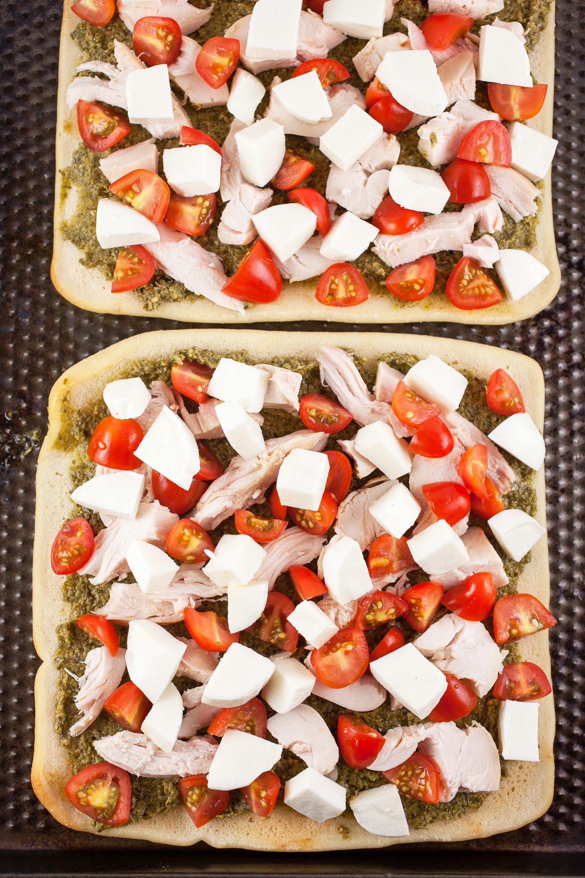 Uncooked flatbread pizzas on baking sheet.