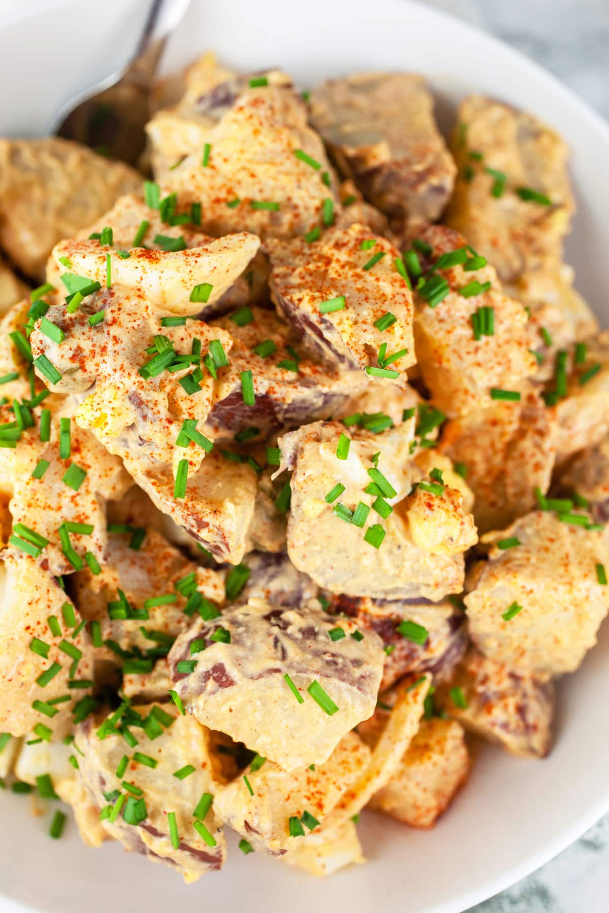 Spanish potato salad with chives in white bowl.