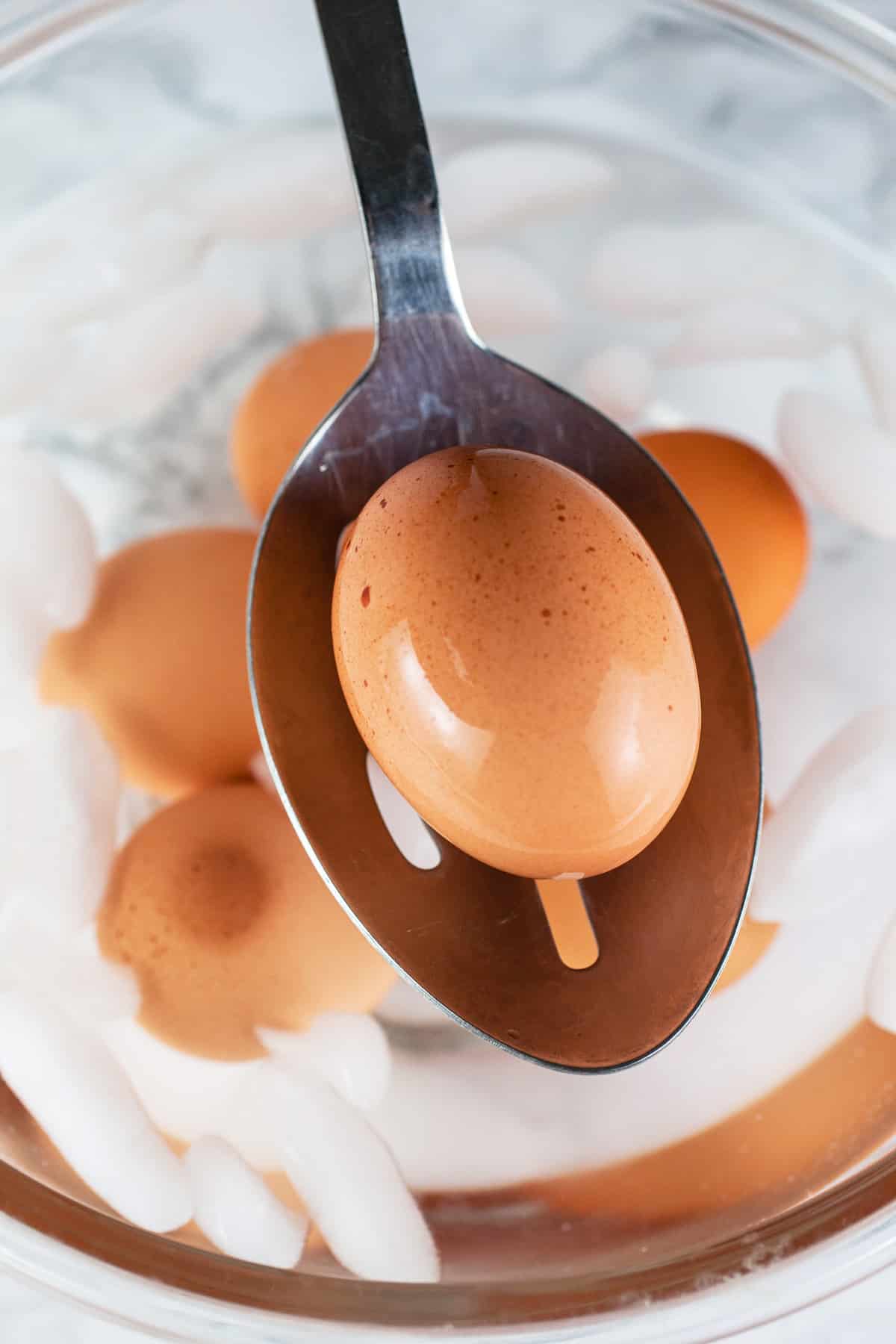 Hard boiled egg on metal slotted spoon lifted from ice bath.