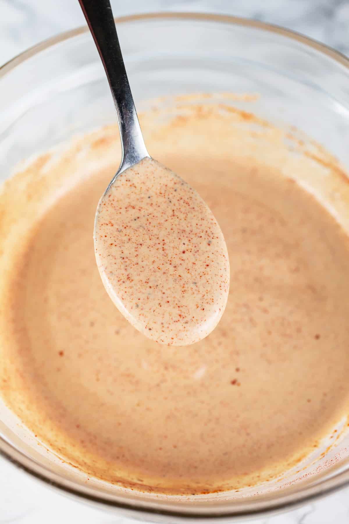 Spoonful of smoked paprika mayo dressing lifted from small glass bowl.